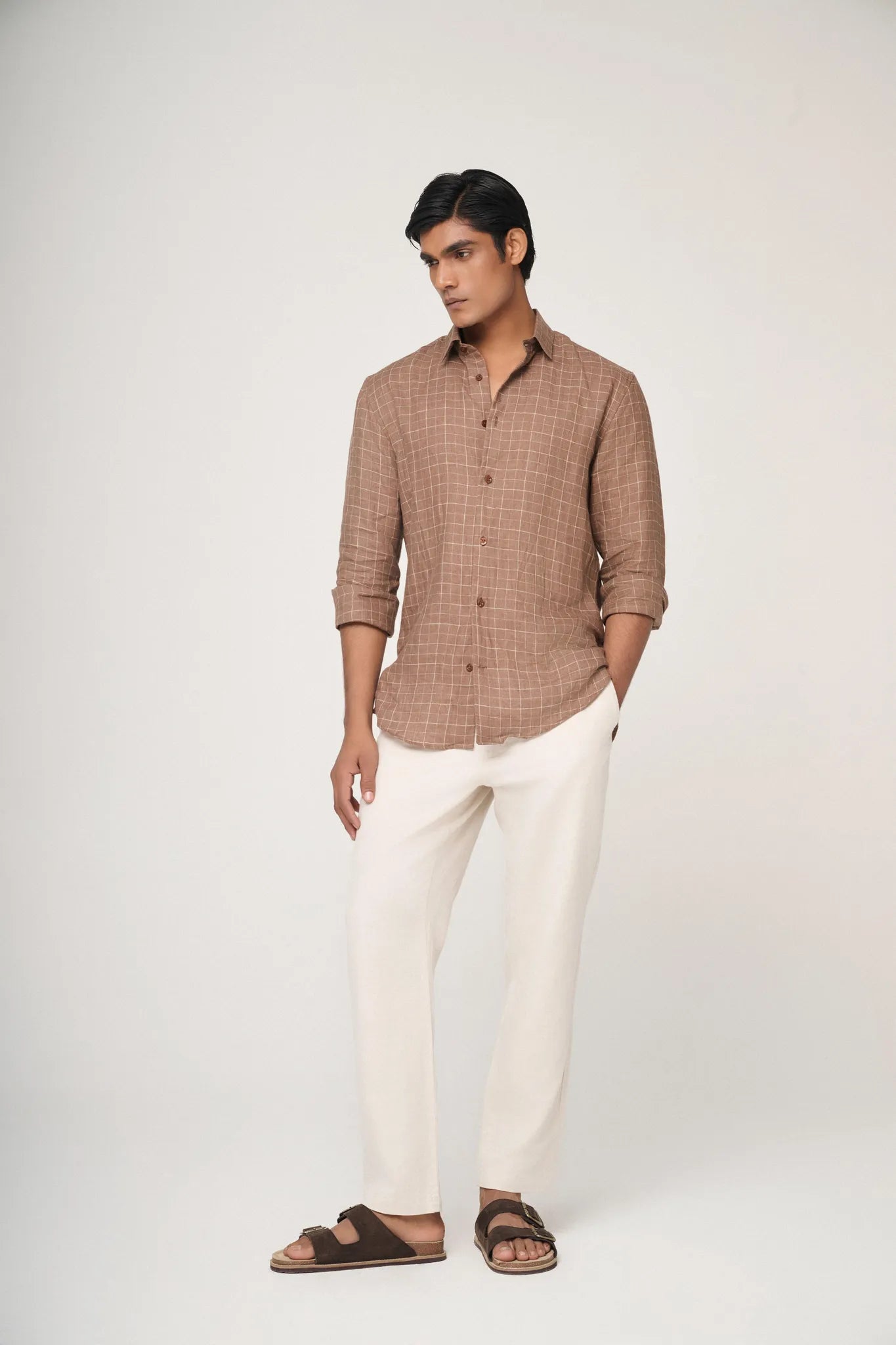 brown checked linen shirt paired with beige trousers.